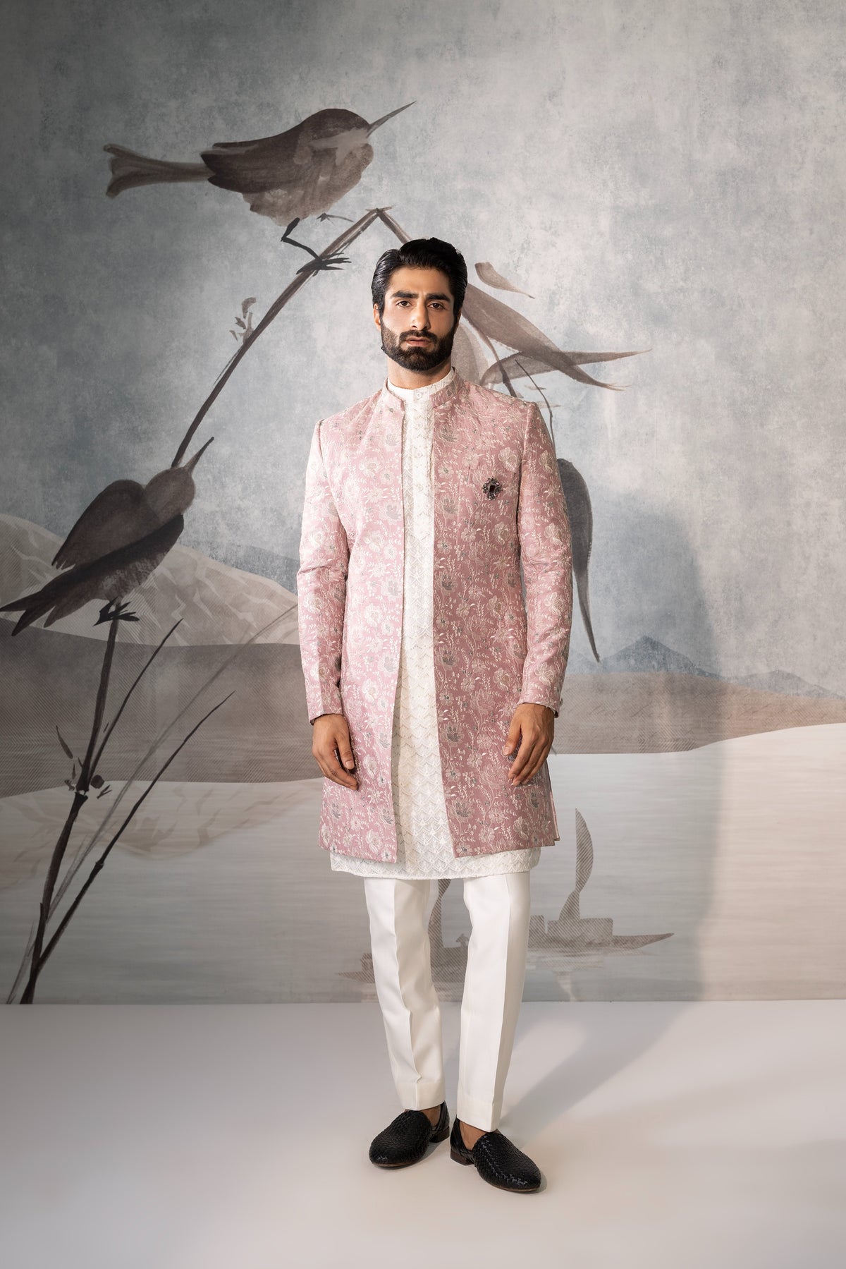 Man wearing a pink sherwani with white pants against a neutral background