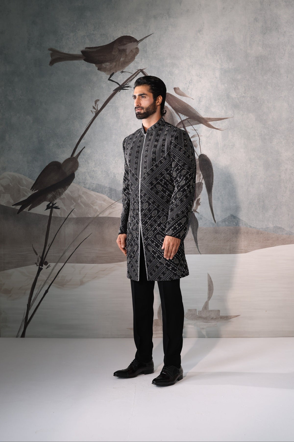 Man in a patterned shirt standing in front of a wall with bird artwork