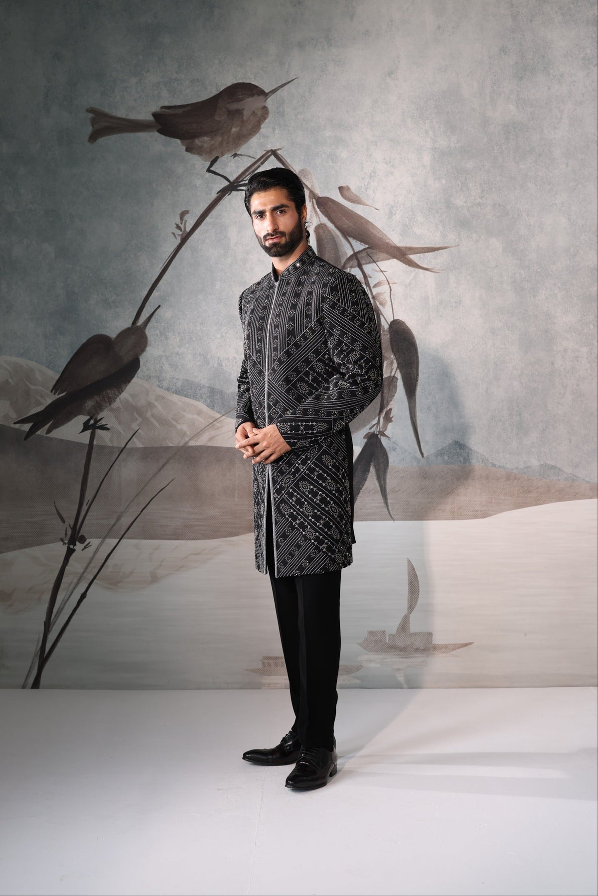 Man in a patterned outfit standing in front of a decorative wall with birds.