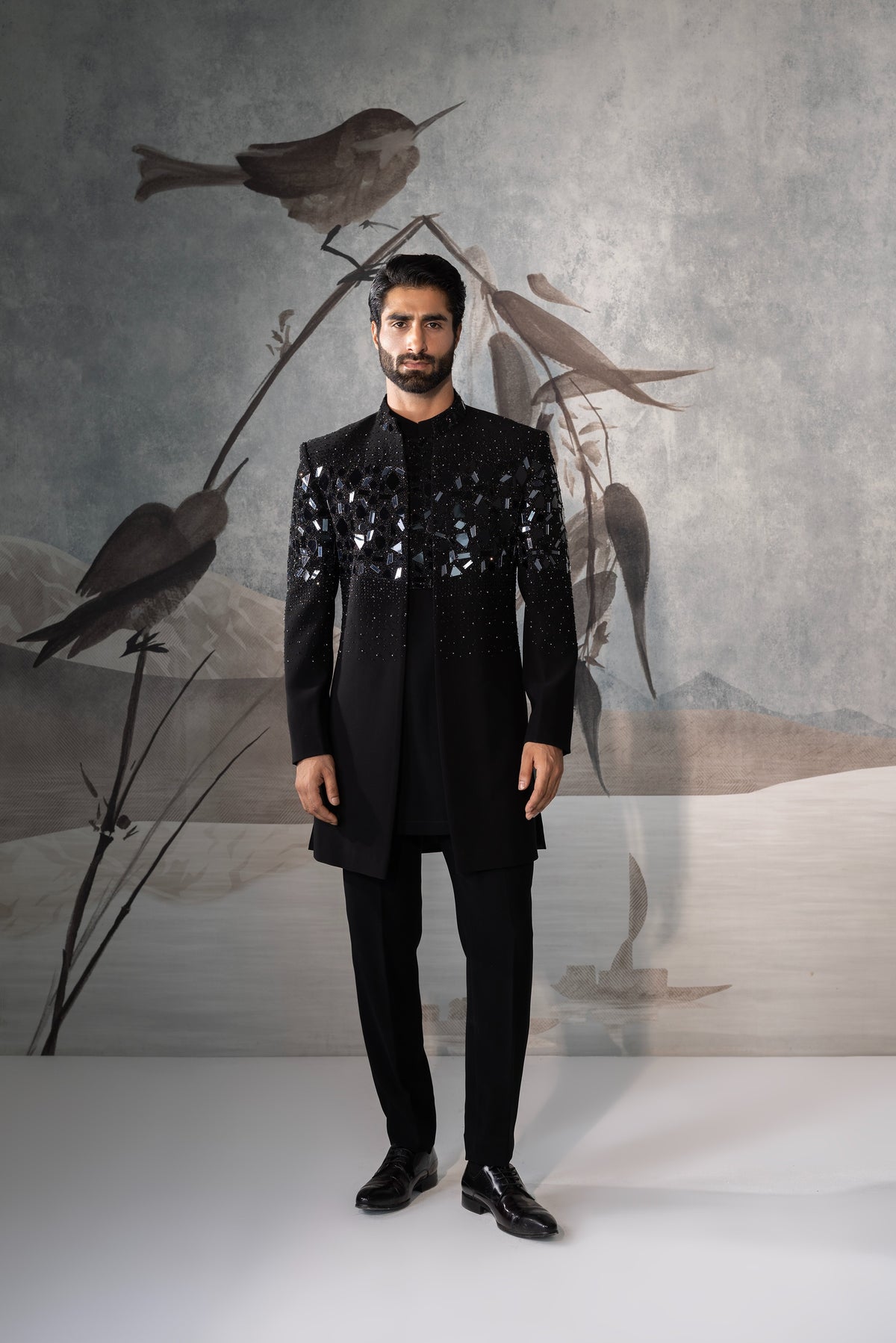Man in a black outfit standing against a backdrop with stylized bird illustrations.