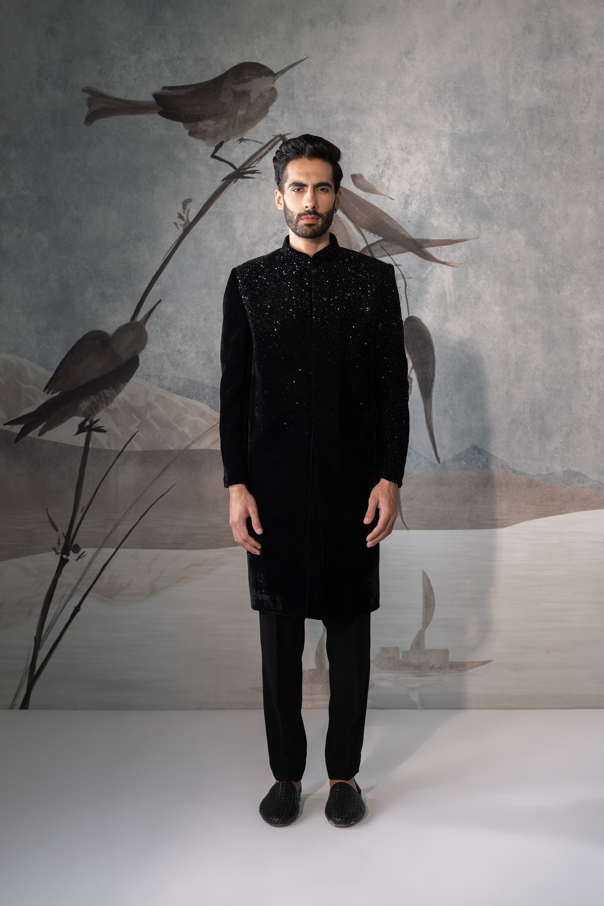 Man wearing a black traditional outfit with a stylized bird illustration in the background
