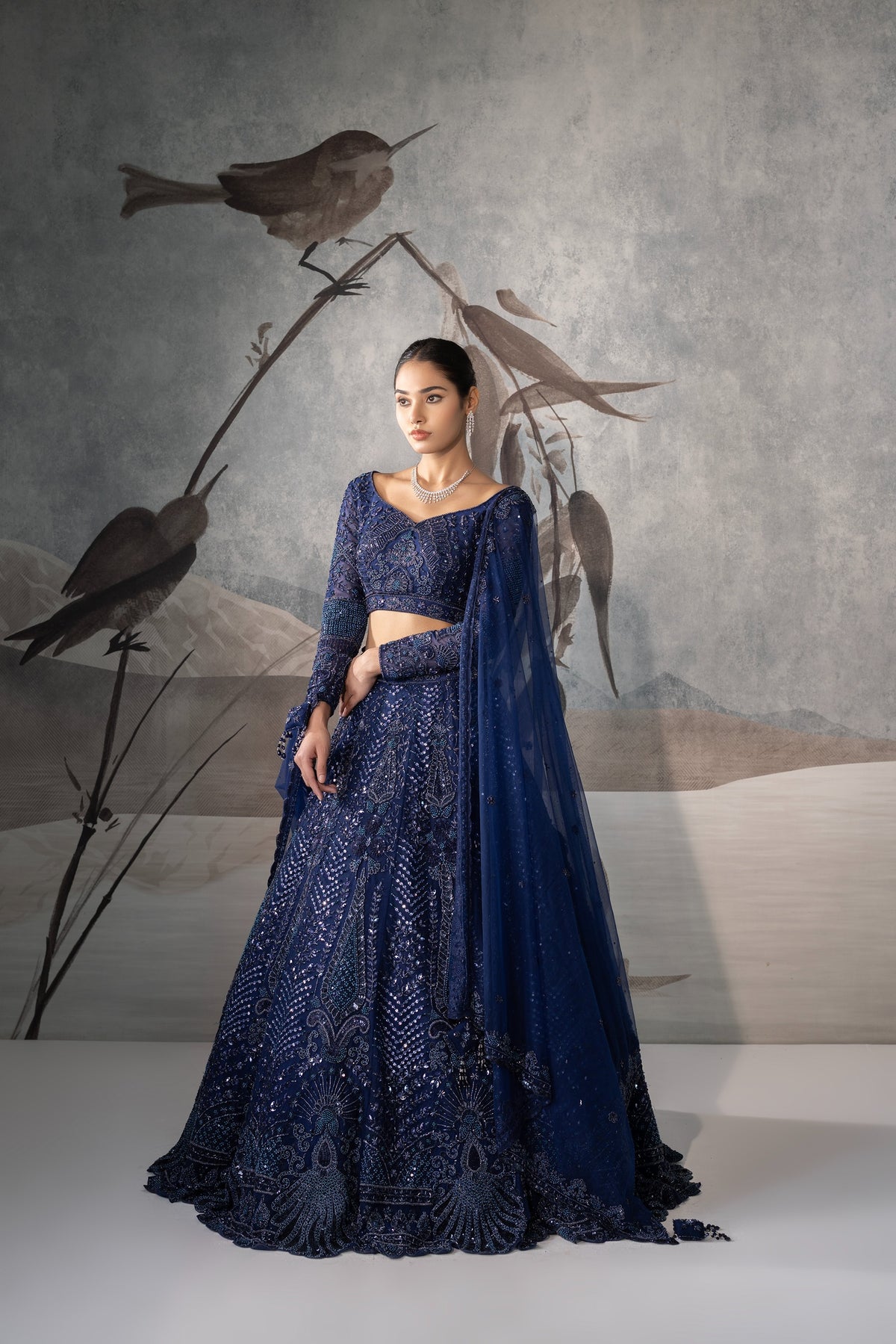 Woman in a blue embroidered outfit standing against a wall with bird artwork.