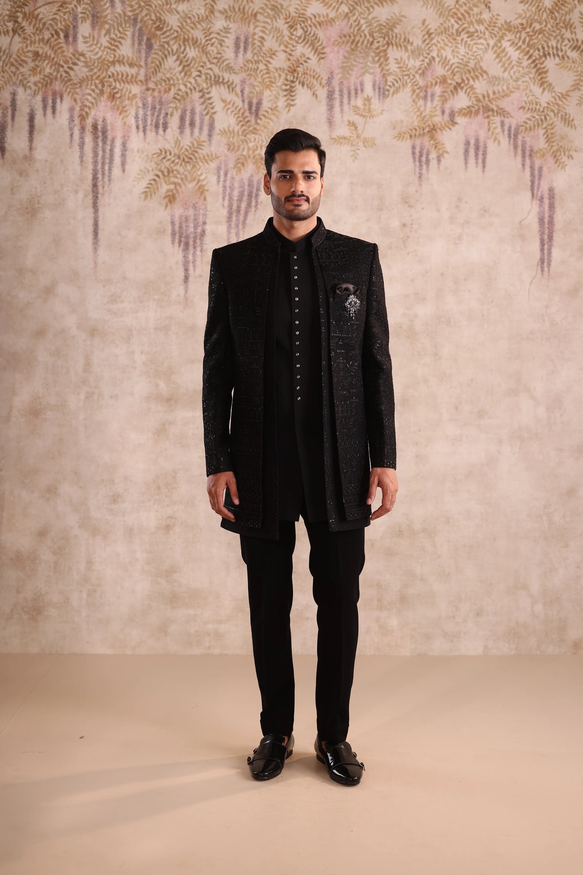 Man wearing a black traditional outfit against a decorative wall.