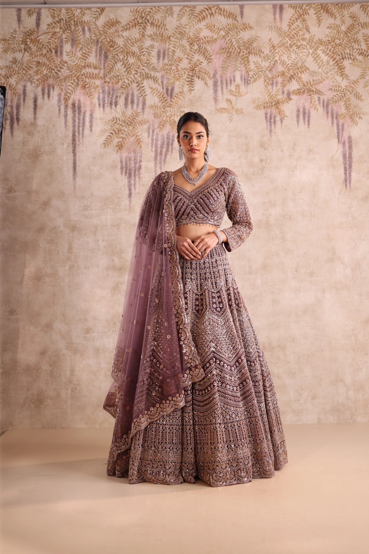 Woman in a traditional outfit with intricate patterns against a decorative wall.