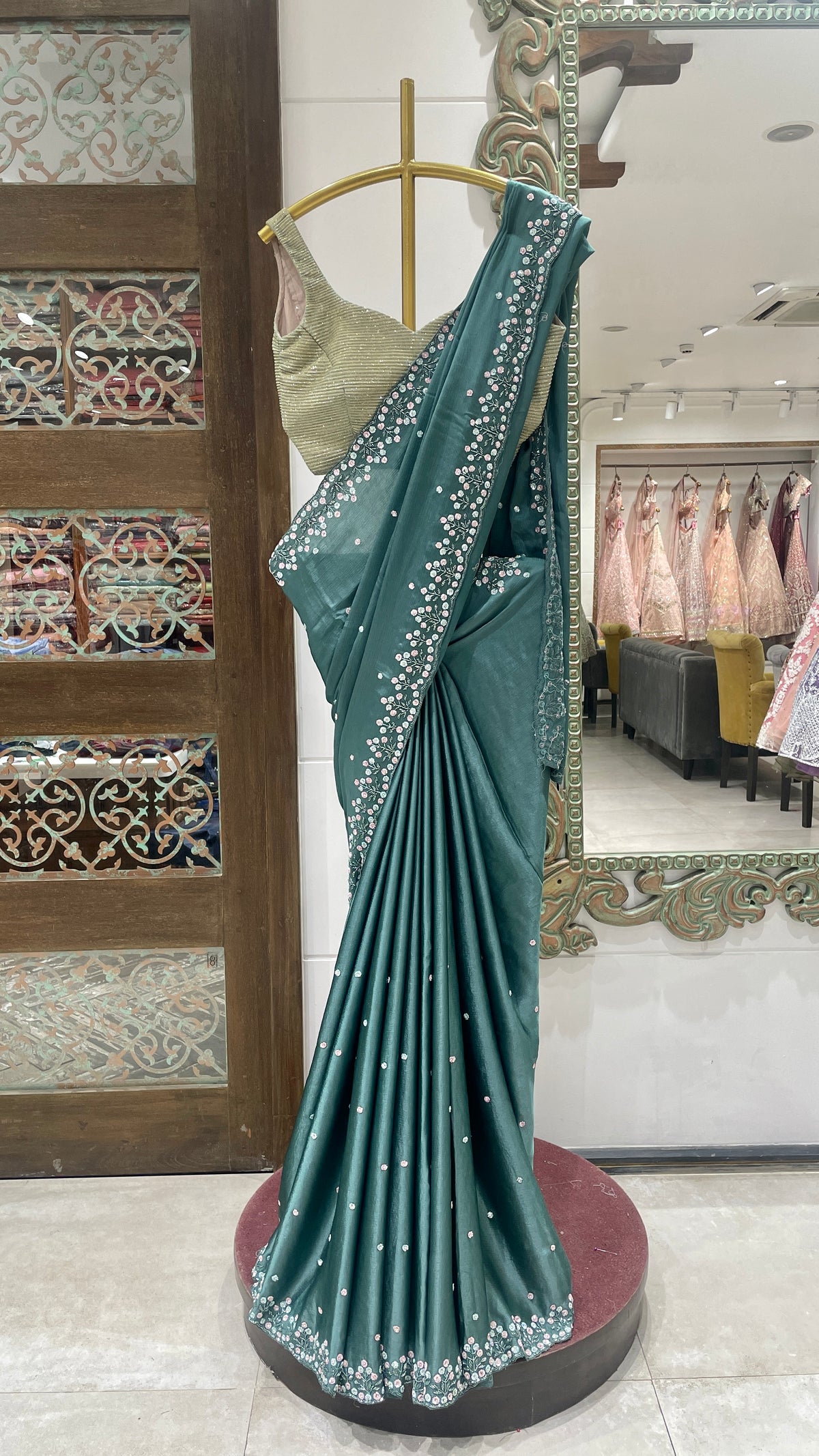 A green crepe saree with floral motifs displayed on a mannequin in a store with intricate floral patterns and a red base.