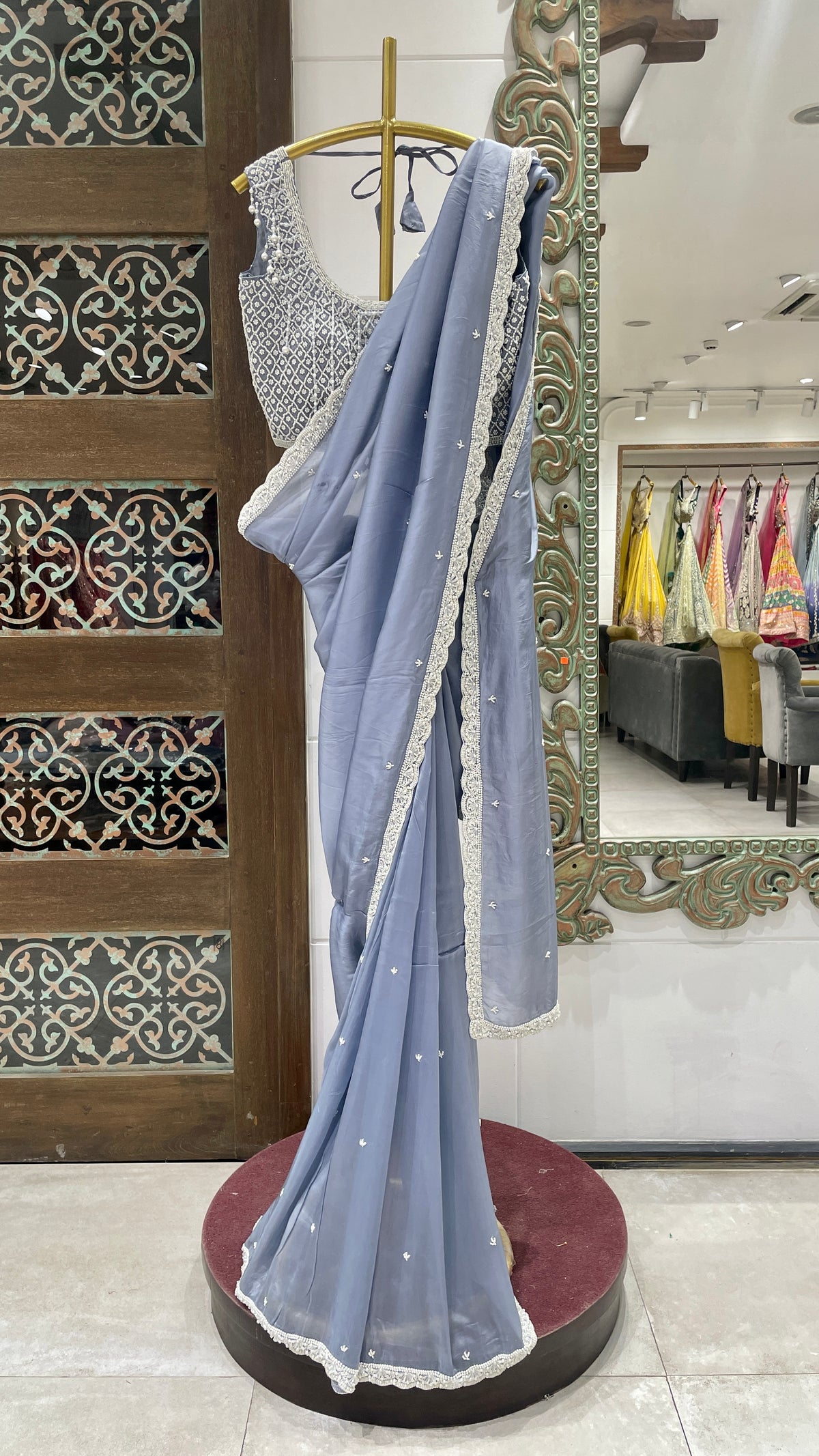 A lilac crape saree with pearl embellishments displayed on a mannequin in a store with various other sarees in the background.