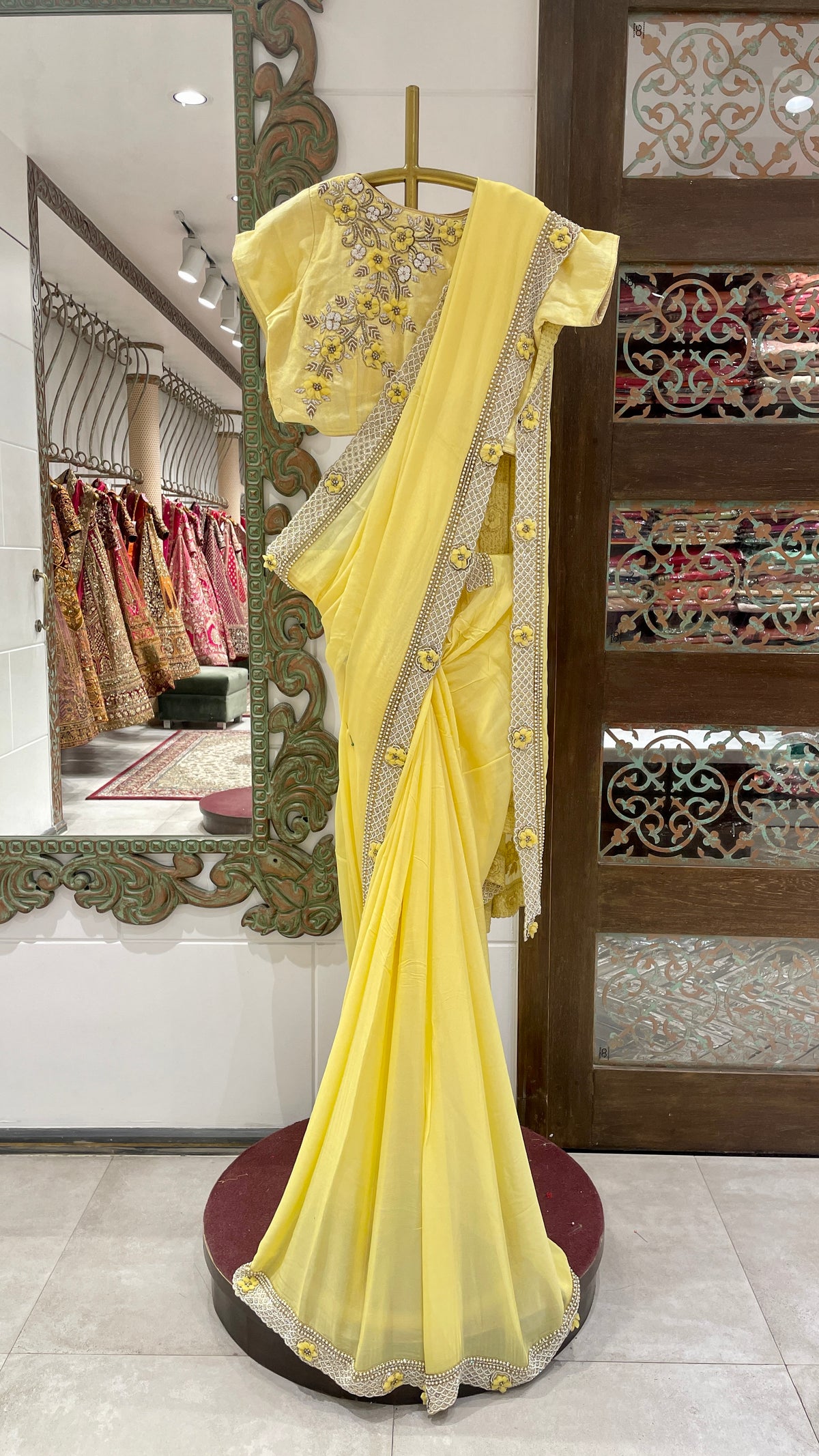 A yellow georgette saree with floral motifs displayed on a mannequin in a store with elaborate floral patterns and a bright yellow color.