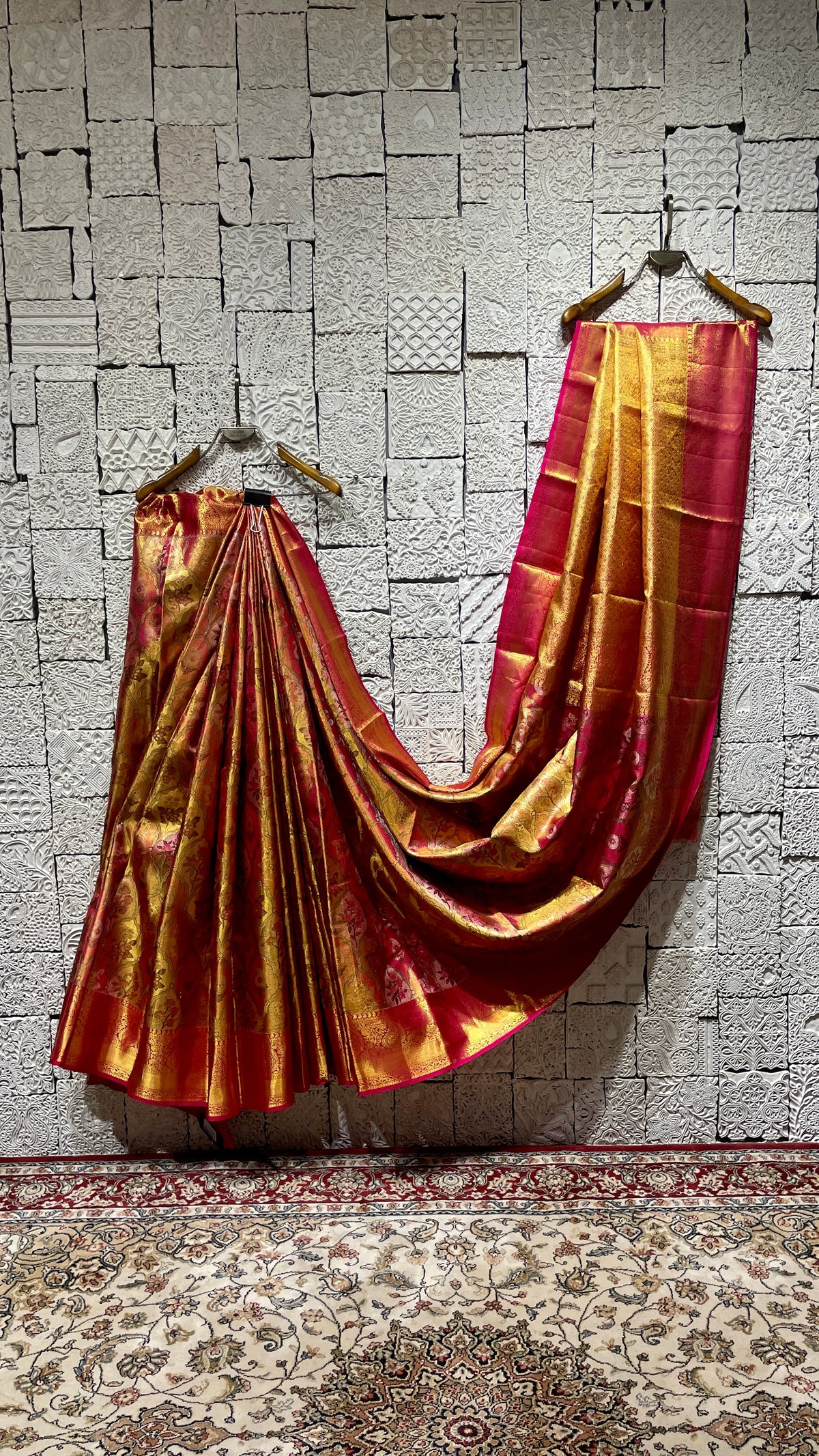 A draped pink silk kanjivaram saree on display with zari work and traditional motifs, hanging against a textured background.