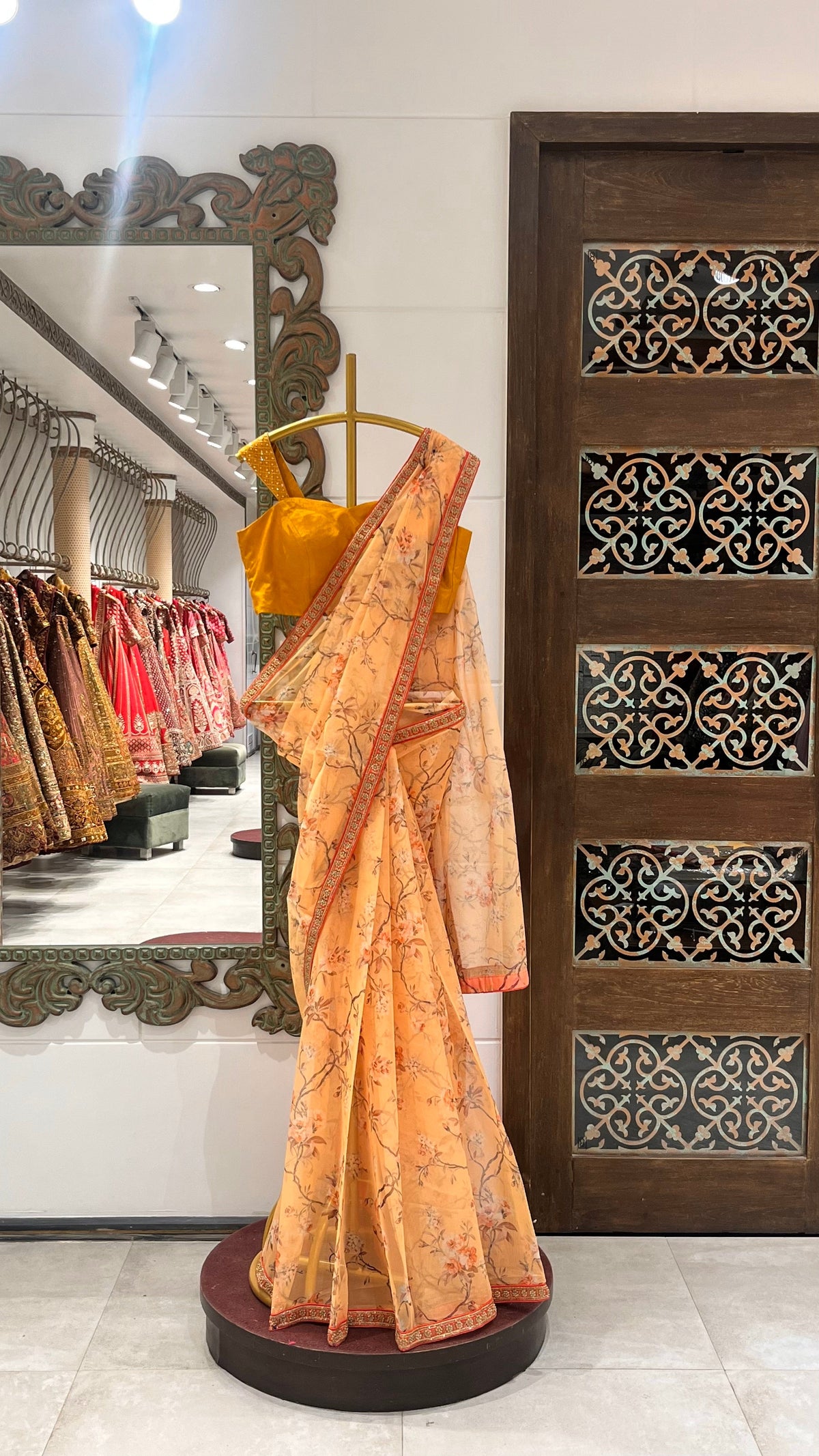 A peach blossom saree draped over a mannequin, featuring floral motifs and a flowing pallu, displayed in a store with traditional attire.