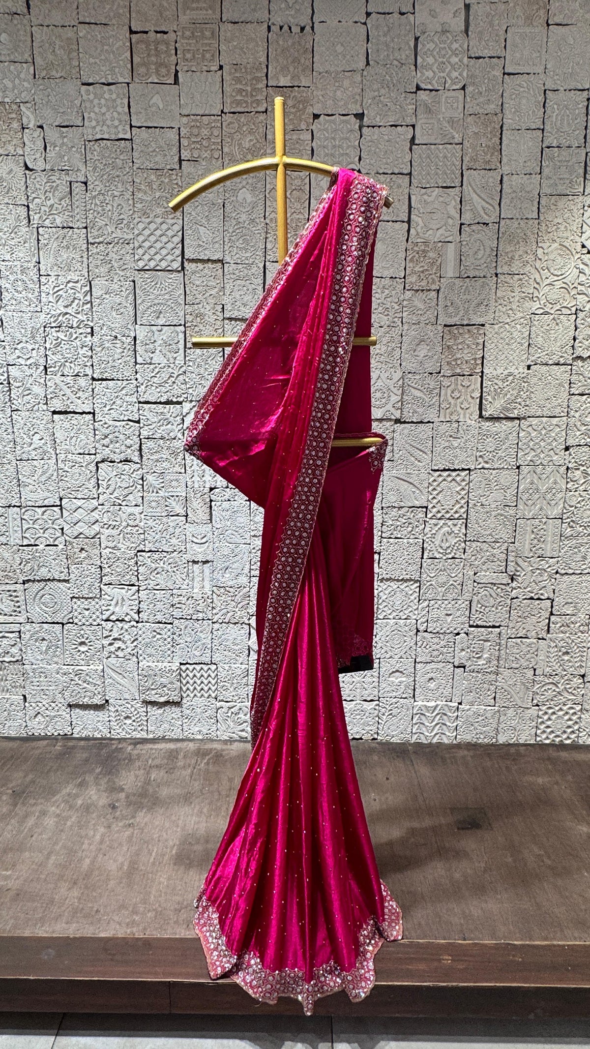 A hot pink saree with pebbles embroidery displayed on a hanger against a brick wall background.