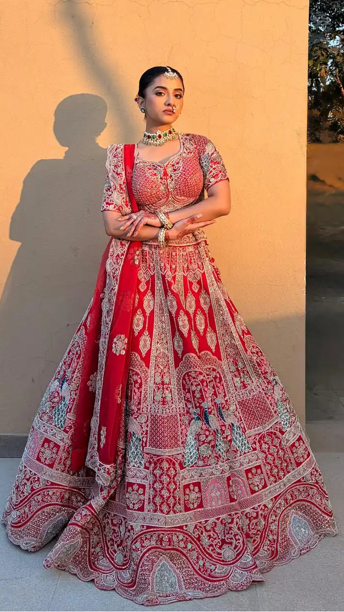 Woman in a red and white traditional outfit standing against a beige wall with an archway.