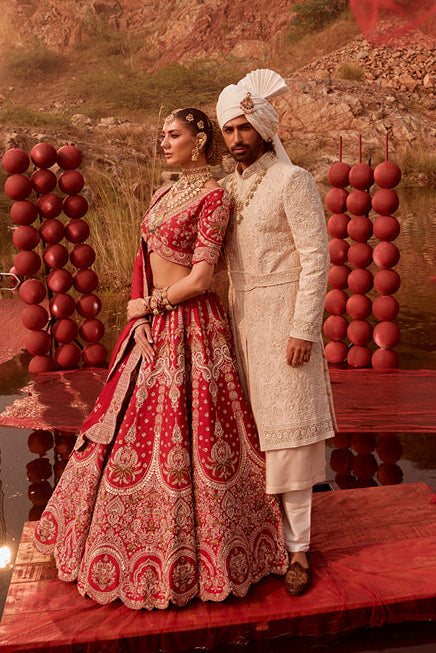 Couple in traditional attire standing on a platform with red decorations and a scenic background.