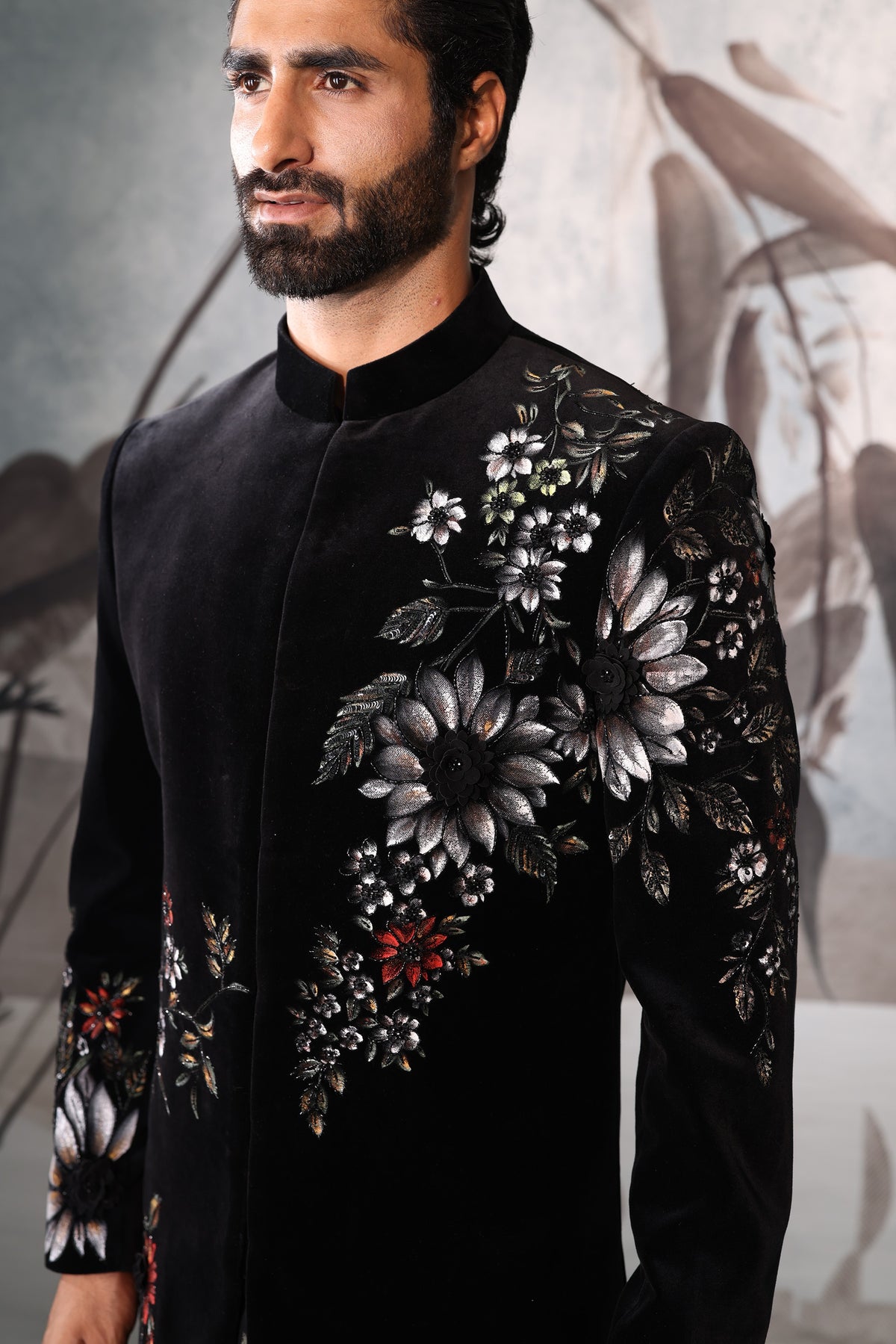 Man wearing a black embroidered jacket with floral patterns against a neutral background