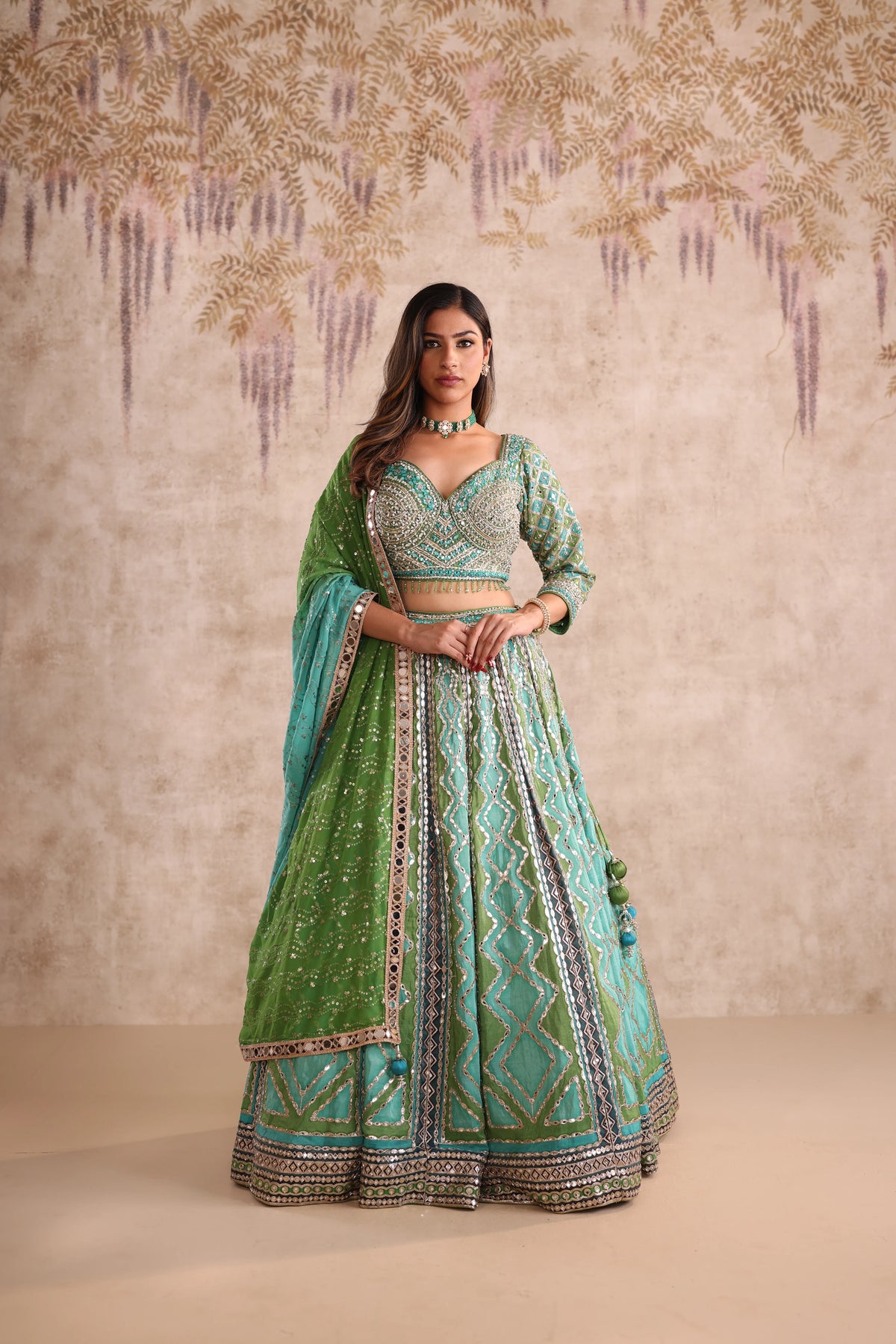 Woman in a green and blue embroidered traditional outfit against a decorative background
