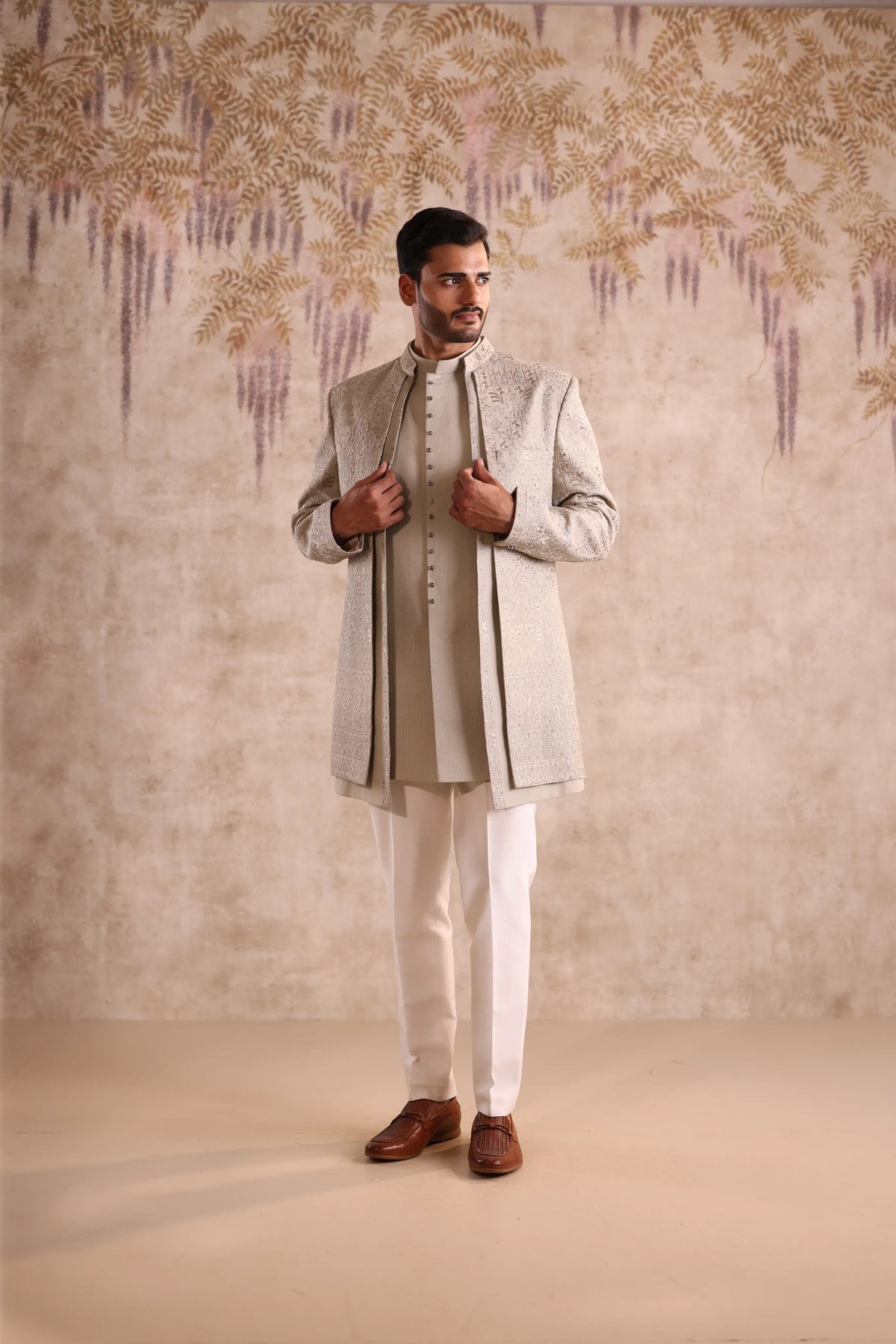 Man wearing a traditional outfit with a textured wall background