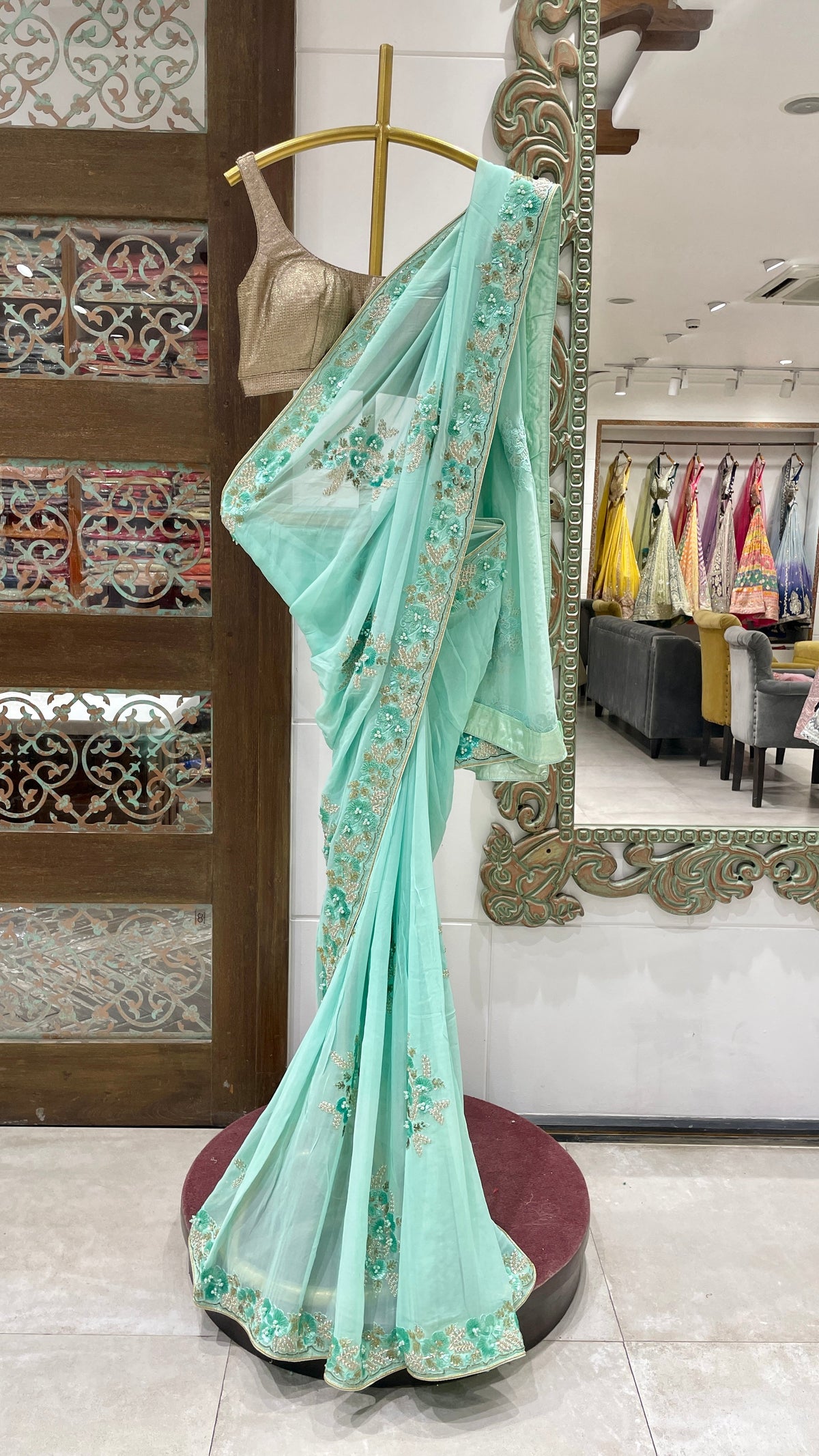 A blue georgette saree with sequins embellishments displayed on a mannequin in a store with various colorful outfits in the background.