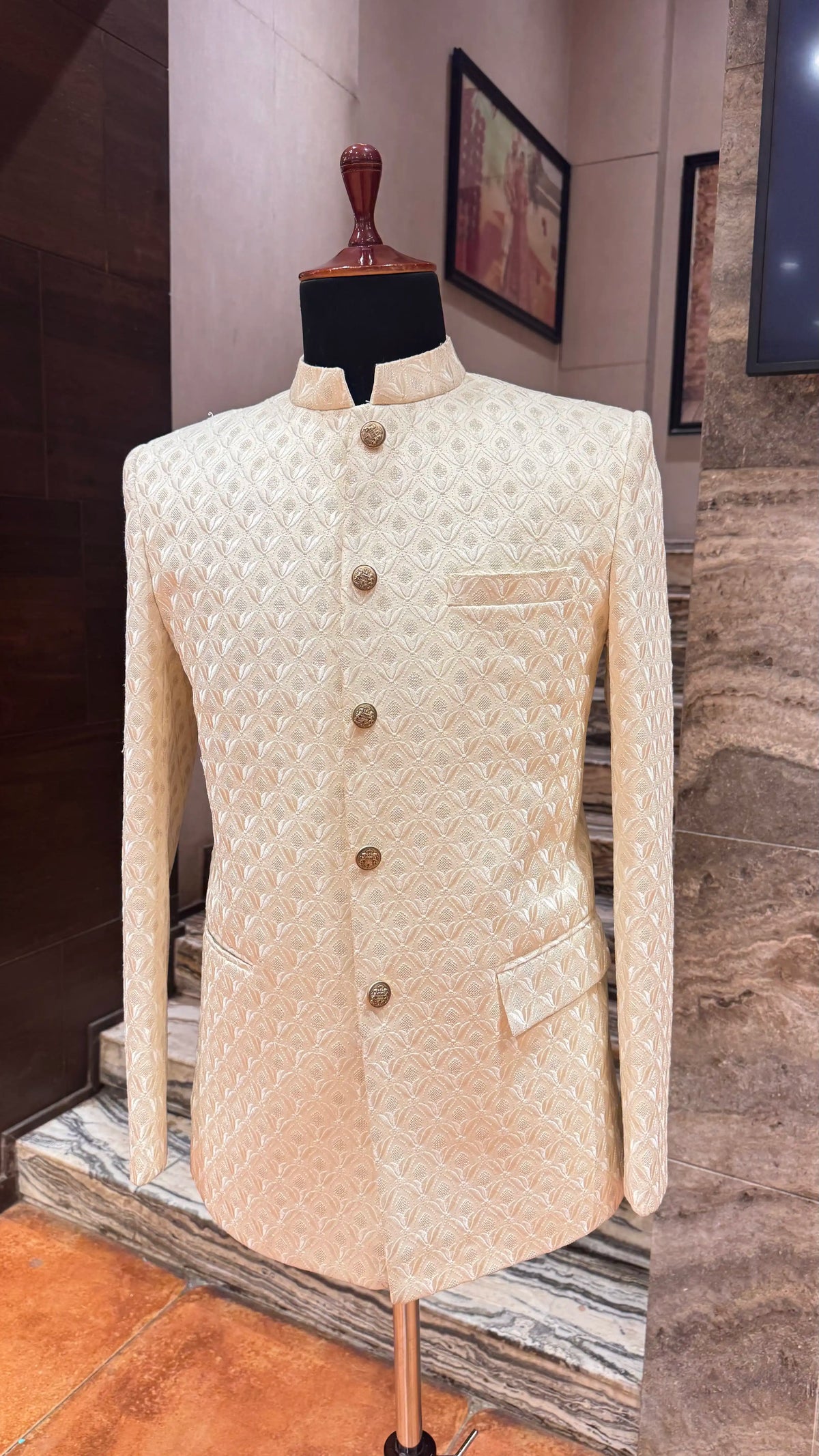 Beige patterned jacket on a mannequin against a marble wall.