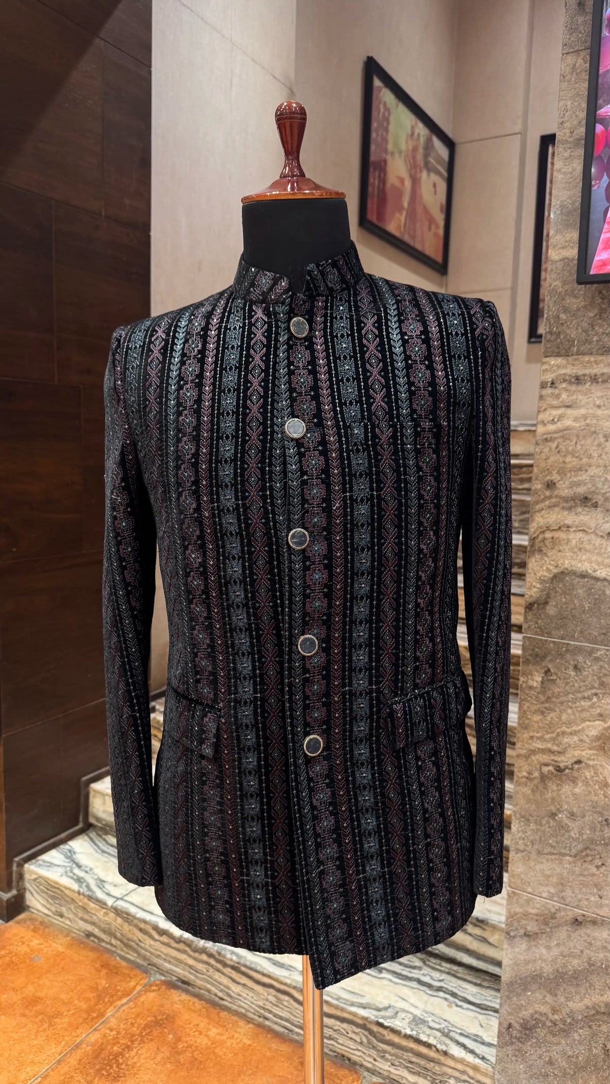 Black patterned jacket on a mannequin against a stone wall.